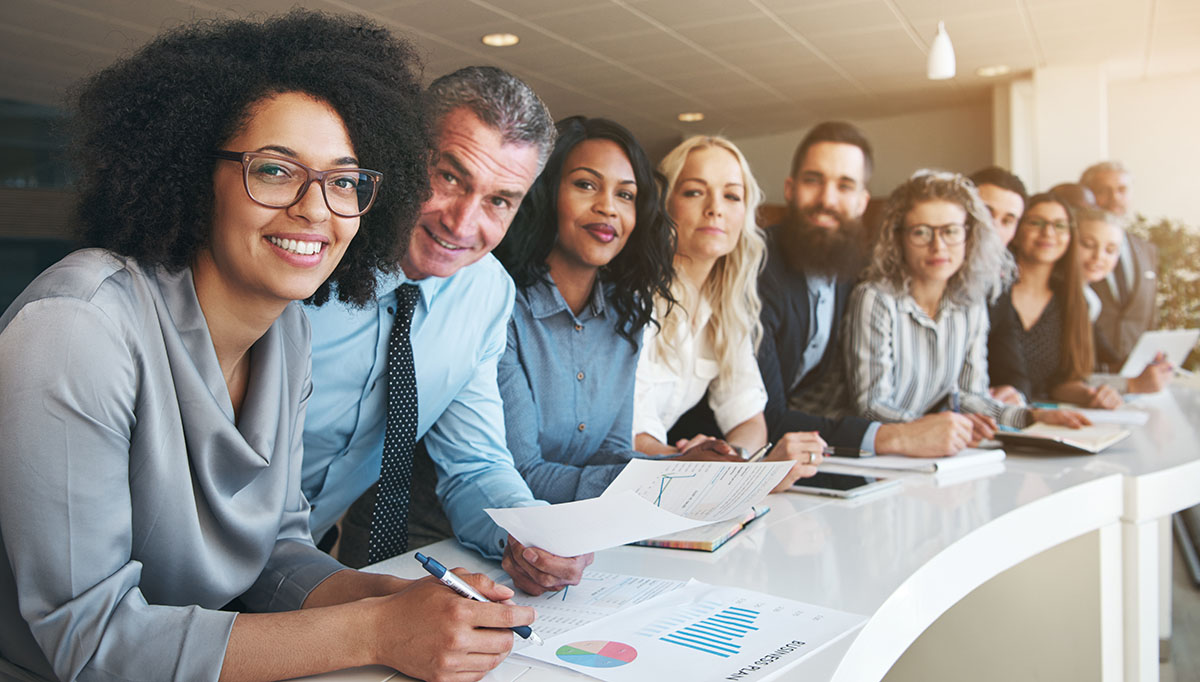 Portrait of a smiling group of diverse corporate colleagues standing in a row together at a table in a bright modern office